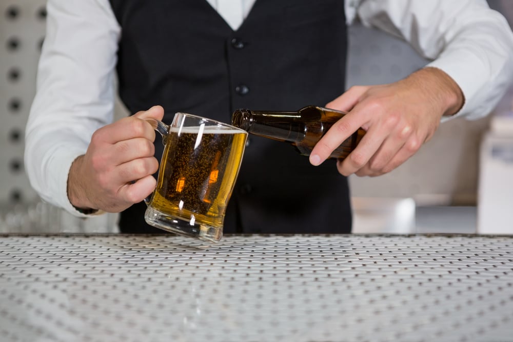 Mid section of bartender pouring beer on glass in bar counter